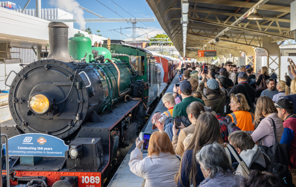 Crowds line a station platform, taking photos of a green steam locomotive (Queensland Rail 1089) during a “Celebrating 160 years” event.